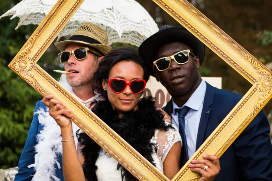 Trois invités posant avec un cadre doré et des accessoires lors d'une soirée