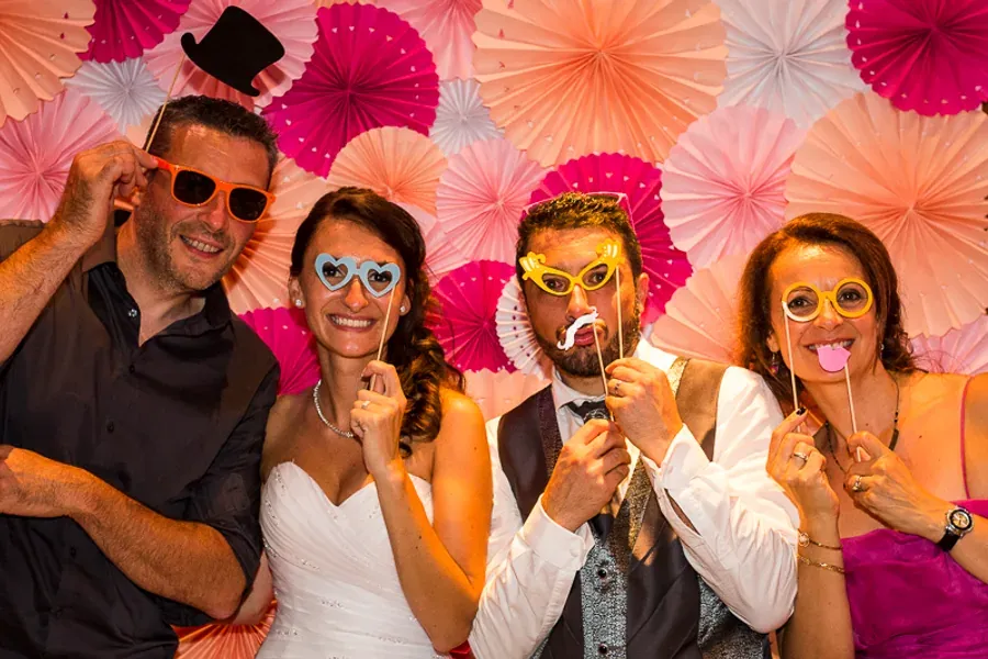 Mariés et invités posant avec des accessoires devant un fond coloré